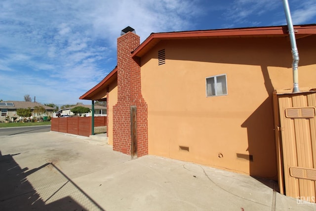 view of side of home with a chimney, stucco siding, crawl space, a patio area, and fence