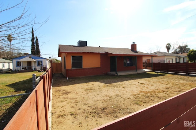 rear view of property featuring a yard, a fenced backyard, a chimney, and a patio