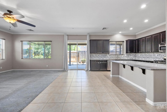 15420 Saint Clement Way, Bakersfield, CA 93314 - kitchen featuring stainless steel microwave, healthy amount of natural light, crown molding, decorative backsplash, and a breakfast bar