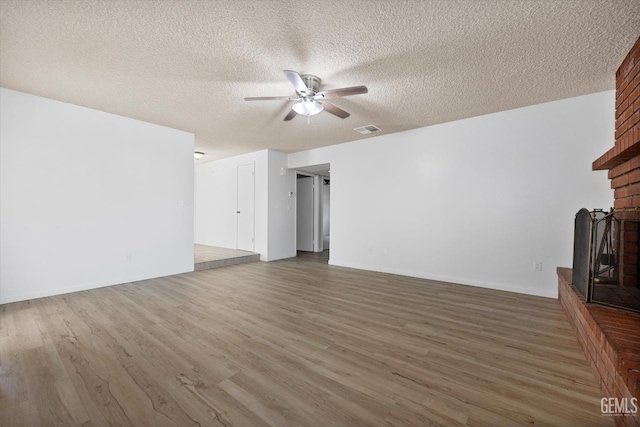 unfurnished living room featuring a fireplace, a textured ceiling, ceiling fan, and dark wood-type flooring