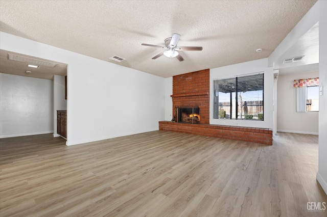 unfurnished living room with ceiling fan, light hardwood / wood-style floors, a textured ceiling, and a brick fireplace