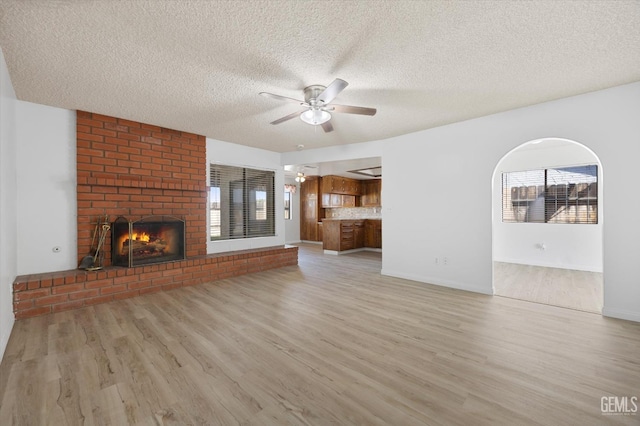 unfurnished living room with ceiling fan, light hardwood / wood-style floors, a textured ceiling, and a brick fireplace