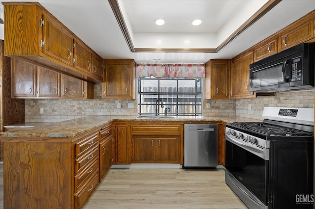 kitchen featuring appliances with stainless steel finishes, light wood-type flooring, tasteful backsplash, a tray ceiling, and sink