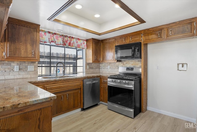 kitchen with light stone countertops, stainless steel appliances, a tray ceiling, sink, and light hardwood / wood-style flooring