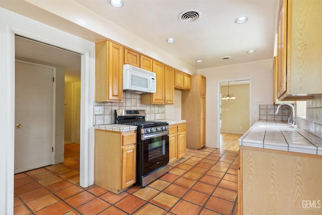 kitchen with tile countertops, tasteful backsplash, a sink, stainless steel gas range, and white microwave