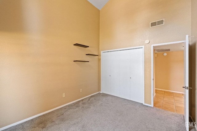 unfurnished bedroom with carpet floors, tile patterned flooring, high vaulted ceiling, and visible vents