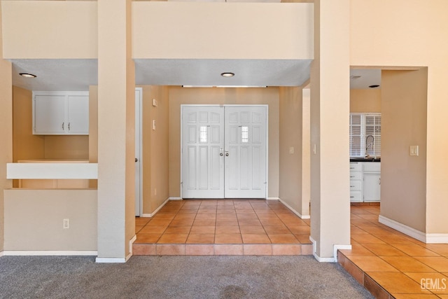 foyer with baseboards, light tile patterned flooring, and light colored carpet