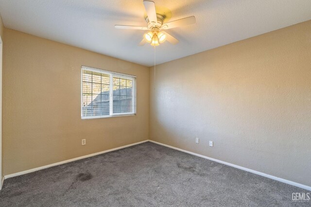 empty room with ceiling fan, dark colored carpet, and baseboards