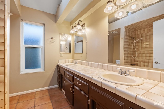 full bathroom featuring a sink, a tile shower, baseboards, and double vanity