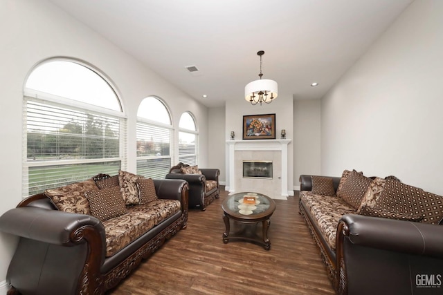 living room with dark wood-type flooring, a tiled fireplace, and an inviting chandelier