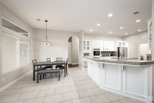 kitchen with pendant lighting, white cabinets, oven, decorative backsplash, and stainless steel fridge with ice dispenser