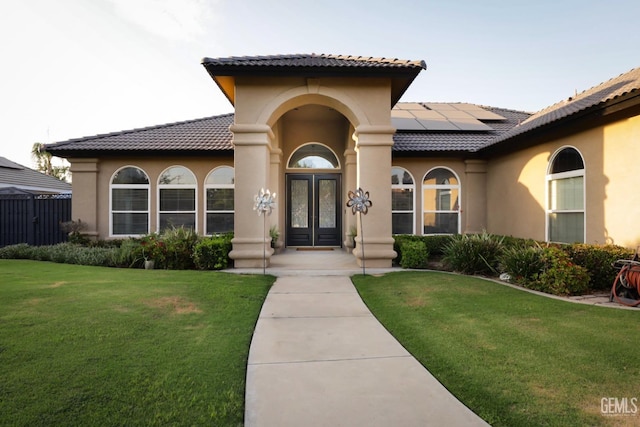 view of exterior entry featuring a lawn, french doors, and solar panels