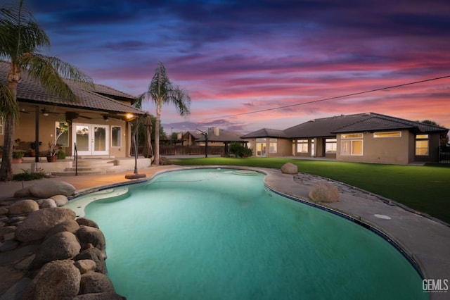 pool at dusk featuring french doors, a yard, ceiling fan, and a patio area