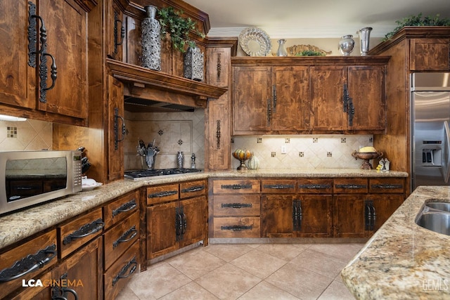 kitchen with light tile patterned floors, tasteful backsplash, appliances with stainless steel finishes, light stone counters, and crown molding