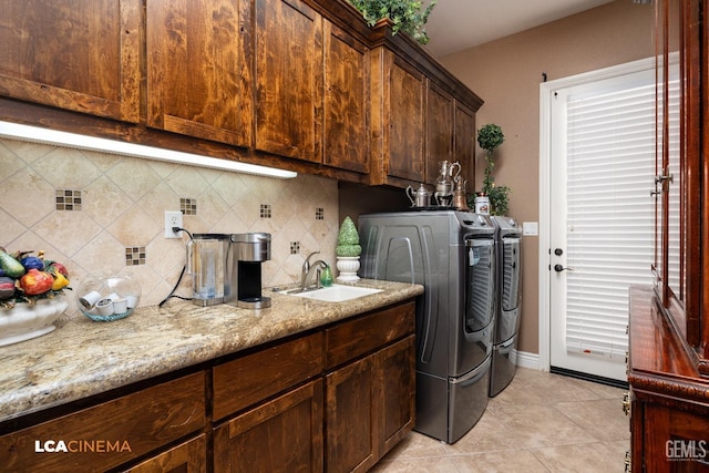 laundry area featuring washing machine and clothes dryer, light tile patterned floors, cabinet space, a sink, and baseboards