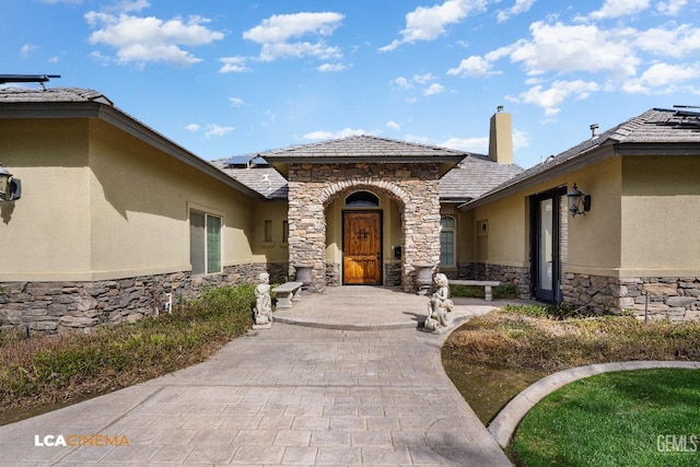 view of exterior entry featuring stone siding, a chimney, and stucco siding