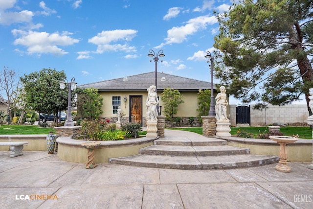 exterior space featuring stone siding, a tiled roof, a gate, fence, and stucco siding