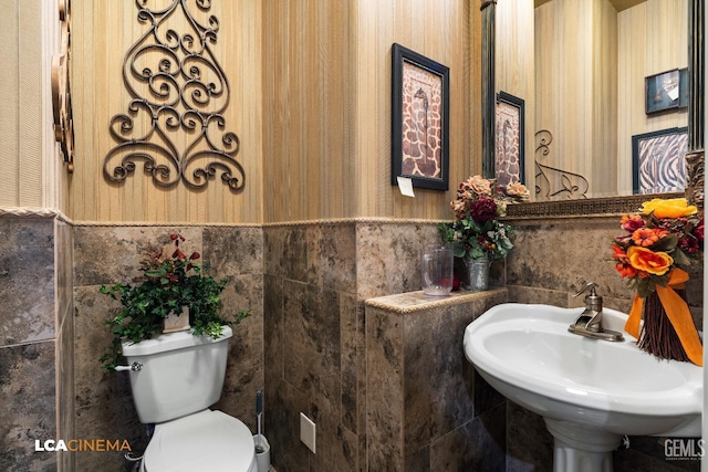 half bathroom with a sink, toilet, tile walls, and wainscoting