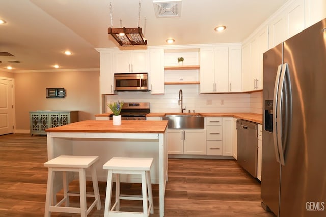 kitchen featuring white cabinets, a kitchen breakfast bar, sink, appliances with stainless steel finishes, and butcher block countertops