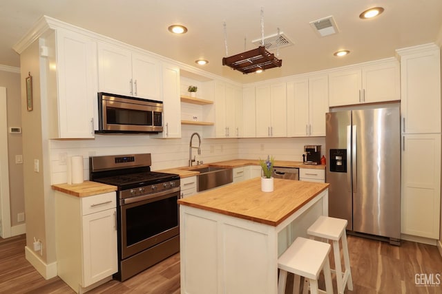 kitchen featuring a center island, wooden counters, sink, appliances with stainless steel finishes, and white cabinetry