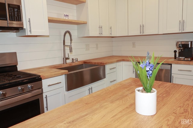 kitchen featuring wood counters, sink, wooden walls, white cabinetry, and stainless steel appliances