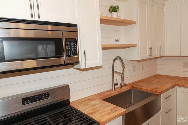 kitchen with butcher block counters, white cabinetry, stove, and sink