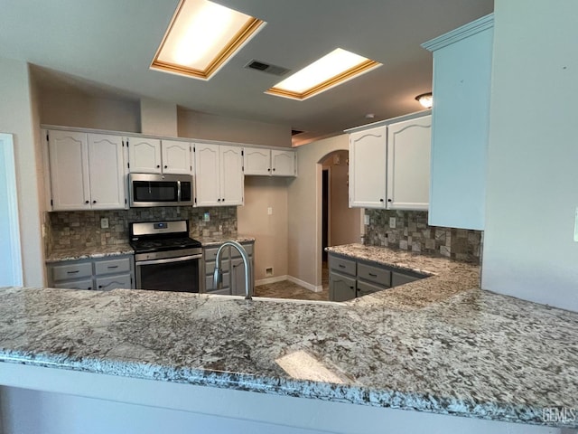 12007 Roaring River Ave, Bakersfield, CA 93311 - kitchen with stainless steel appliances, arched walkways, a sink, tasteful backsplash, and white cabinetry