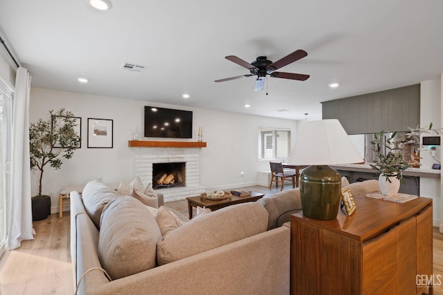 living room featuring ceiling fan, a brick fireplace, and light wood-type flooring