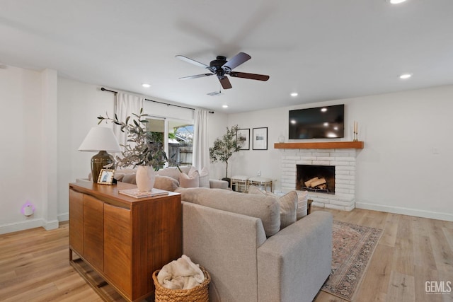 living room featuring ceiling fan, a fireplace, and light wood-type flooring