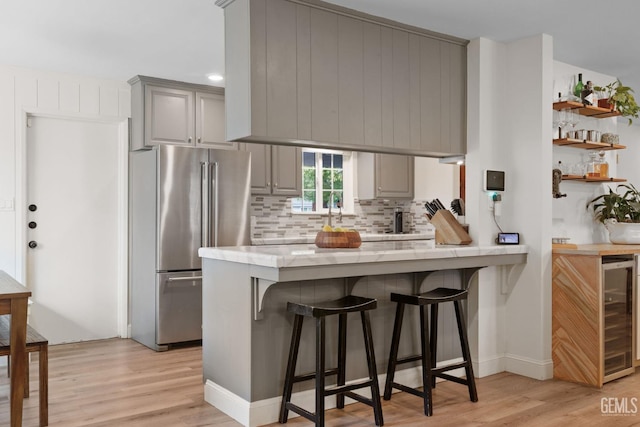 kitchen with gray cabinets, a breakfast bar, high end refrigerator, wine cooler, and kitchen peninsula