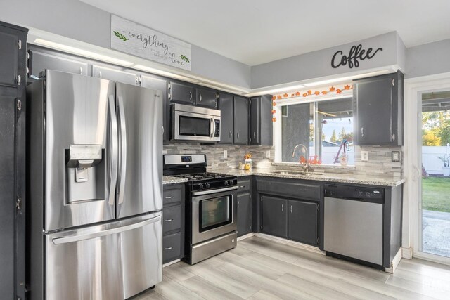 kitchen with decorative backsplash, stainless steel appliances, light stone counters, and sink