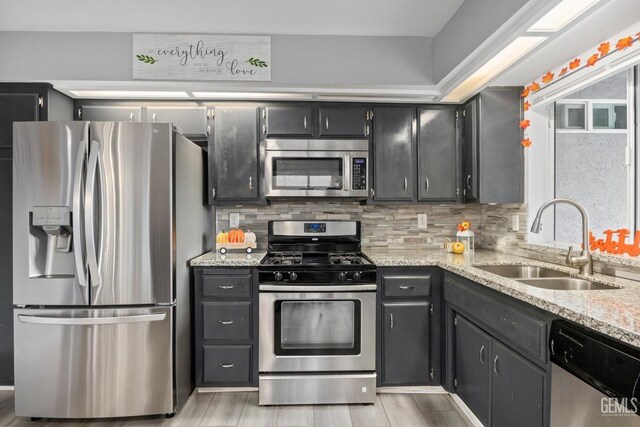 kitchen featuring appliances with stainless steel finishes, backsplash, light stone counters, and sink