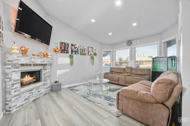 living room with a stone fireplace, light wood-type flooring, and a textured ceiling