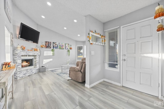 foyer entrance featuring a stone fireplace, a textured ceiling, and light wood-type flooring