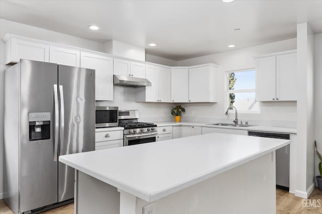 kitchen with stainless steel appliances, under cabinet range hood, white cabinets, and a sink