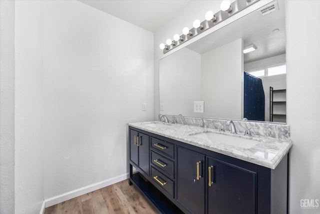 full bathroom with double vanity, visible vents, a sink, and wood finished floors
