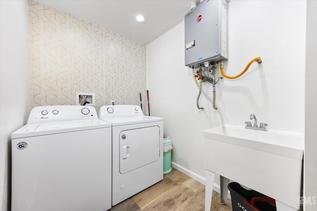 washroom featuring water heater, an accent wall, laundry area, washer and dryer, and light wood finished floors