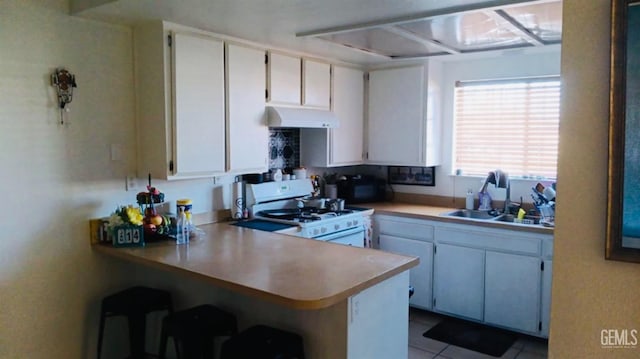 kitchen featuring kitchen peninsula, sink, light tile patterned flooring, white cabinetry, and white range with gas stovetop