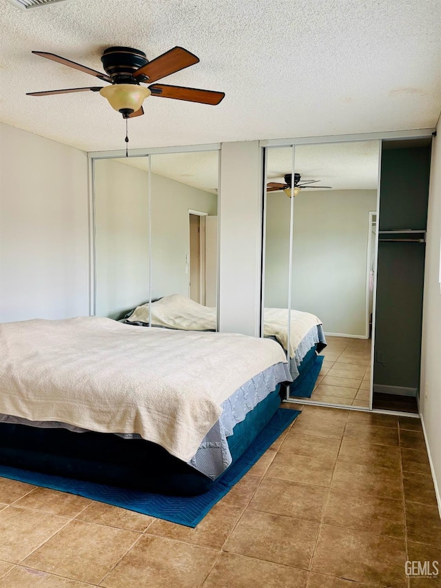 bedroom featuring tile patterned flooring, two closets, baseboards, a textured ceiling, and a ceiling fan