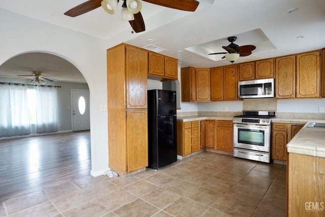 kitchen with a tray ceiling, a ceiling fan, light countertops, and stainless steel appliances