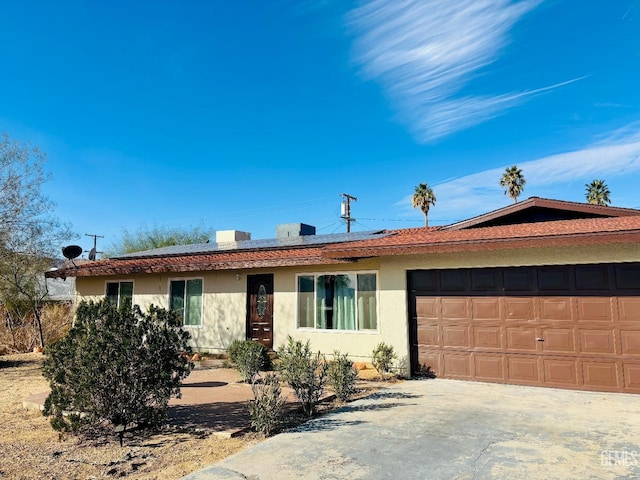 ranch-style home featuring stucco siding, roof mounted solar panels, concrete driveway, and an attached garage