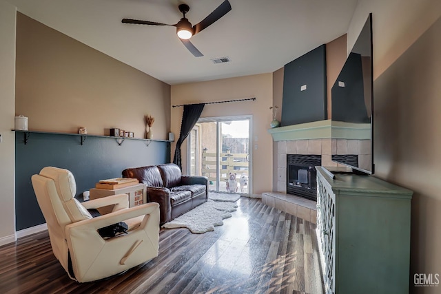 living room featuring a tile fireplace, dark hardwood / wood-style floors, and ceiling fan