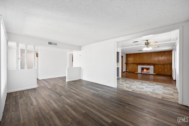 unfurnished living room featuring ceiling fan, dark hardwood / wood-style flooring, a textured ceiling, wooden walls, and a fireplace