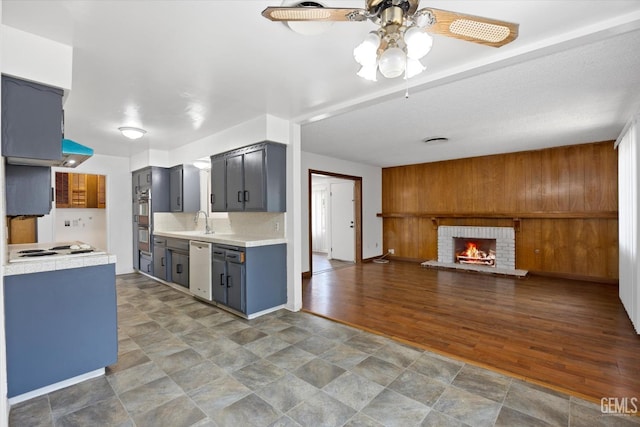 kitchen featuring ceiling fan, sink, stainless steel double oven, a brick fireplace, and white gas stovetop