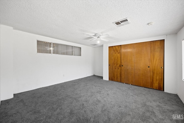 unfurnished bedroom featuring ceiling fan, dark carpet, a textured ceiling, and a closet