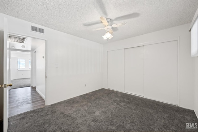 unfurnished bedroom with ceiling fan, a closet, dark carpet, and a textured ceiling