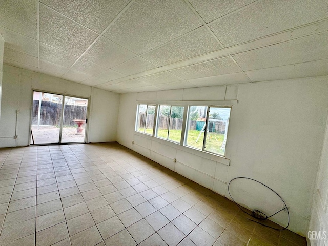 unfurnished room with light tile patterned floors, plenty of natural light, and a paneled ceiling