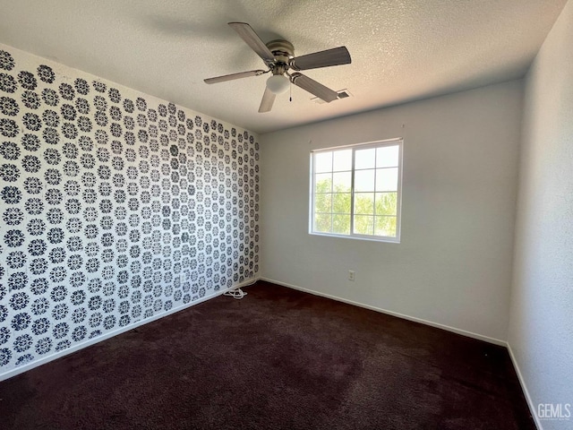 unfurnished room with visible vents, baseboards, dark carpet, a textured ceiling, and a ceiling fan