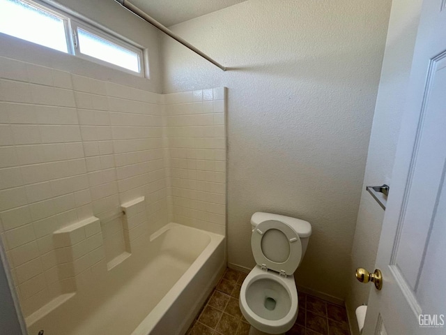 full bath with tile patterned floors, washtub / shower combination, toilet, and a textured wall