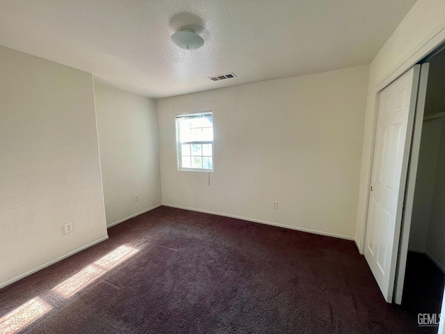 unfurnished bedroom featuring visible vents, dark carpet, a textured ceiling, and baseboards